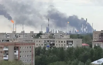 Fire at an oil refinery with thick black smoke against a backdrop of residential buildings, illustrating strikes on Russia's fuel system