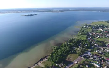 Аэрофотосъемка живописного украинского озера с чистыми водами и зеленым берегом, окруженным деревней — пример природного курорта, не уступающего мировым