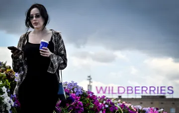 Woman in sunglasses holding a smartphone and coffee in front of the Wildberries logo, illustrating new safety rules for employees
