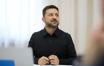 Президент Украины Владимир Зеленский в черной рубашке сидит за столом, задумчиво глядя в сторону, обсуждая стратегию завершения войны до зимы 2026 года.