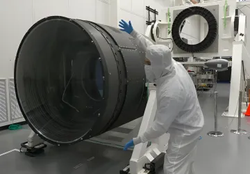 Ingenieur in einem Reinraumanzug inspiziert die riesige Linse der LSST-Kamera im Labor
