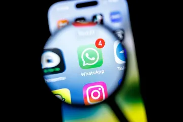 Логотип WhatsApp с уведомлением о новых сообщениях, увеличенный лупой на экране смартфона, символизирующий массовую блокировку аккаунтов и технические сбои в работе мессенджера.