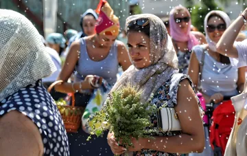 Women with bundles of herbs and apples on a festive street, symbolizing the tradition of harvest gathering for the Saviour festivals in 2026.