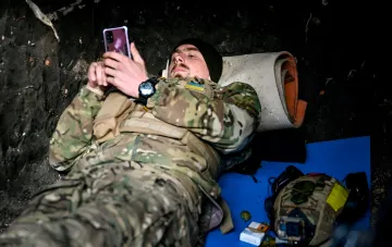 Украинский военнослужащий в окопе смотрит в смартфон, иллюстрируя уязвимость перед кибершпионажем и романтическими ловушками российских спецслужб