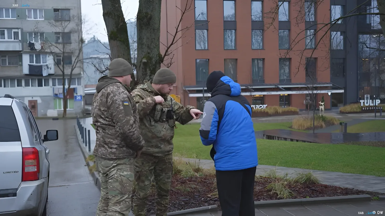 Ukrainian soldiers in camouflage talking to a civilian on a city street, possibly related to the shooting incident at the Odesa TCC