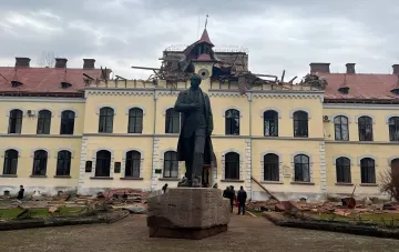 Damaged building with a monument to Stepan Bandera against the backdrop of a destroyed roof