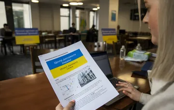 Женщина изучает информационный листок Центра помощи Украине в Белфасте, иллюстрируя сложности с жильем и пенсией для украинцев с инвалидностью в Ирландии