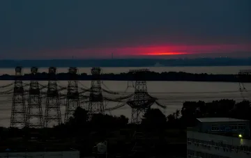 Силуэты опор ЛЭП на фоне заката у Запорожской АЭС, символизирующие утрату внешнего питания