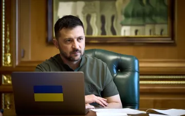 Президент Украины Владимир Зеленский за рабочим столом с ноутбуком, на котором наклеен украинский флаг, обсуждает новые задачи для секретаря СНБО Игоря Клименко.