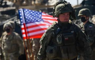 Солдаты армии США с флагом на фоне военной техники, иллюстрирующие тему конфликта с Ираном и дефицит ракет THAAD