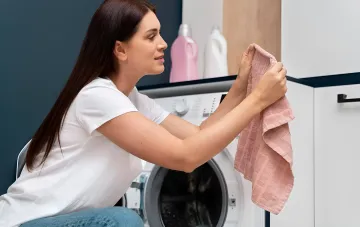 Женщина осматривает чистое полотенце после стирки без кондиционера, демонстрируя результаты эксперимента по экономии средств и заботе о технике