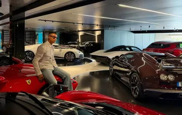 Криштиану Роналду сидит на красном Ferrari в своем роскошном гараже, окруженный суперкарами Bugatti и Lamborghini