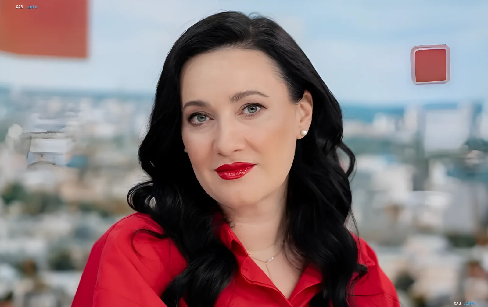 Kateryna Osadcha in a red blouse looking at the camera against a blurred cityscape — symbol of recovery after night attacks