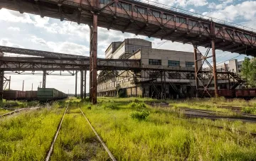 Заброшена вугільна фабрика в Червонограді з зарослими травою залізничними коліями та іржавими конструкціями, що символізує загрозу опалювальному сезону України через вугільну кризу.