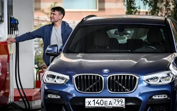 Мужчина заправляет синий BMW на заправке, иллюстрируя тему топливного коллапса в России