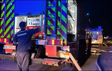 Rescue worker in uniform with 'РЯТУВАЛЬНИК' text working at a fire truck at night on a railway platform after an attack where bodies of the deceased were found