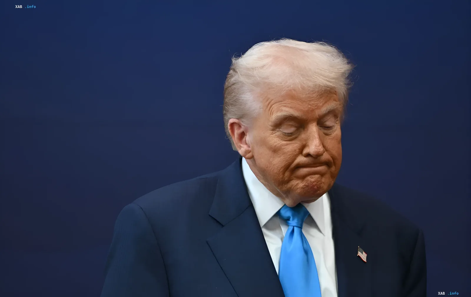 Дональд Трамп в синем костюме с американским флагом на лацкане, задумчивый взгляд, на фоне темно-синего экрана, в контексте задержания вооруженного наблюдателя у его гольф-клуба в Калифорнии
