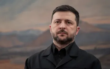 Президент Украины Владимир Зеленский в черной форме на фоне гор, обсуждающий стратегию защиты городов через уничтожение пусковых установок.