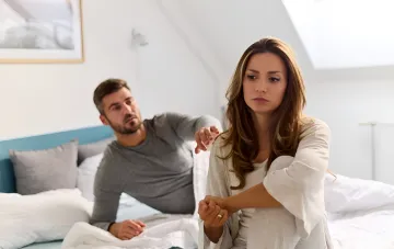 Couple in bed, woman looks offended and turns away, man tries to comfort her — illustration for article about zodiac signs that never forgive offenses