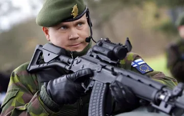 Finnischer Soldat mit Gewehr in Tarnanzug und Barett, der die Verteidigung in sumpfigem Gelände symbolisiert