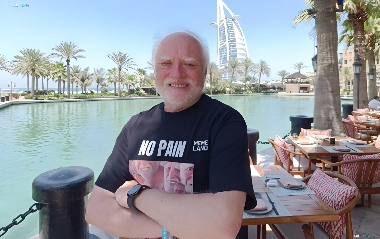Гарольд, инженер из Венгрии, в футболке с надписью 'NO PAIN' и изображением своего лица, сидящий у бассейна с видом на Бурдж-аль-Араб в Дубае