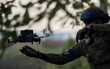 Украинский боец в камуфляже с синей повязкой на шлеме управляет военным дроном — символ обучения иностранных наемников, включая колумбийских бойцов наркокартелей