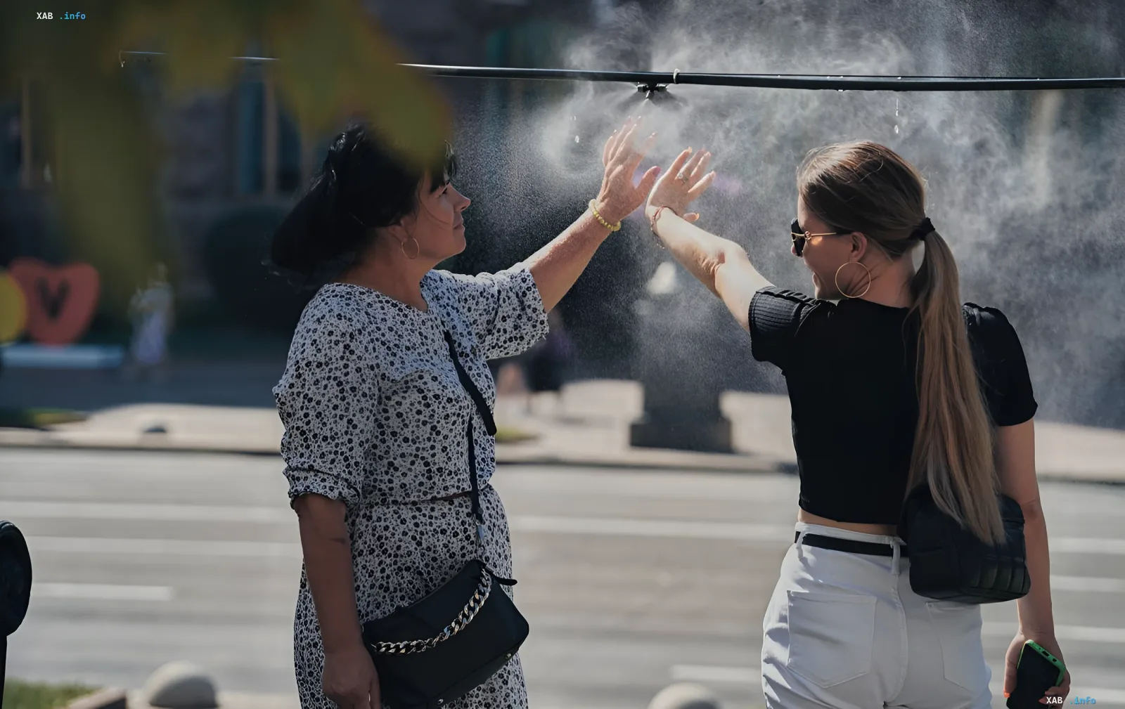 Frauen kühlen sich unter einem Wassersprüher an einem heißen Tag in der Ukraine, die Temperatur erreicht +38°C
