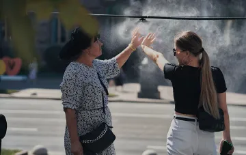 Frauen kühlen sich unter einem Wassersprüher an einem heißen Tag in der Ukraine, die Temperatur erreicht +38°C