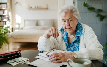 Rentnerin mit Brille studiert Dokumente und Wohnkosten, symbolisiert den Erhalt von VPL-Leistungen während der Arbeit im Jahr 2026