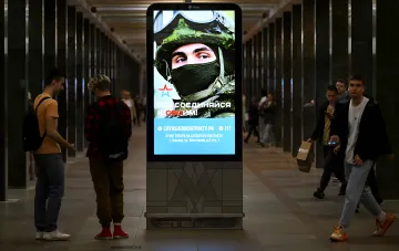 Рекламный щит с призывом к службе по контракту в метро Москвы на фоне проходящих людей, иллюстрирующий контраст между государственной пропагандой и снижением общественного одобрения войны по данным «Левада-центра»