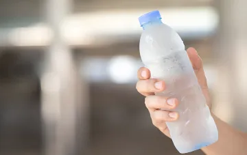 Gefrorene Wasserflasche in der Hand als selbstgemachter Klimagerät zur Kühlung bei Hitze