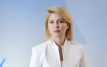 Olga Stefanischina, ehemalige ukrainische Botschafterin in den USA, in einem weißen Anzug vor einem blauen Himmel, im Kontext des Falls der illegalen Bereicherung