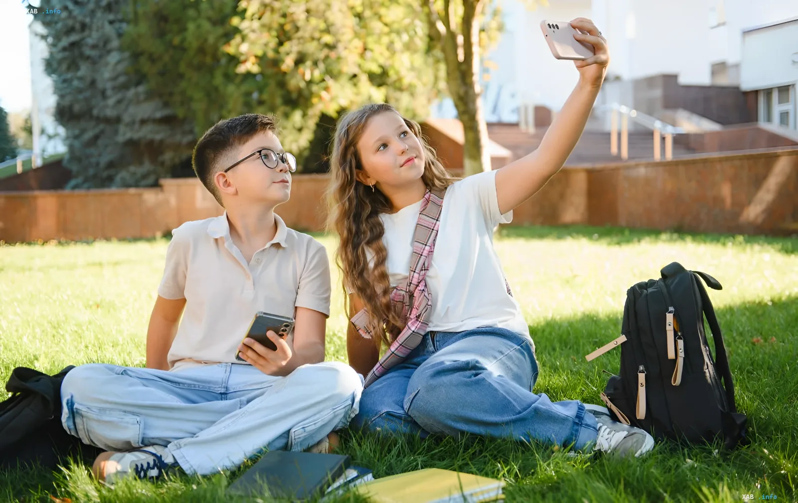 Schüler machen ein Selfie mit einem Smartphone auf Gras mit Rucksäcken und Schulbüchern, illustrieren das Thema Tech-Rucksack und notwendige Gadgets für Schüler