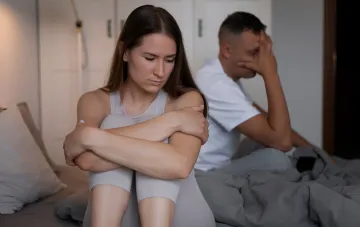Couple sitting back-to-back in bed, expressing emotional detachment — visualizing the concept of 'quiet divorce'
