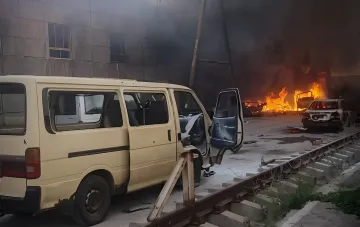 Aftermath of 'Bandera' strike on Ukrposhta depot in Pavlohrad: burning cars and damaged van against smoky building backdrop