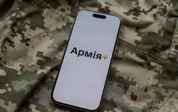 Smartphone displaying the 'Army+' app logo on screen, resting on camouflage fabric — symbolizing digitalized transfers in the Ukrainian Armed Forces without commander approval