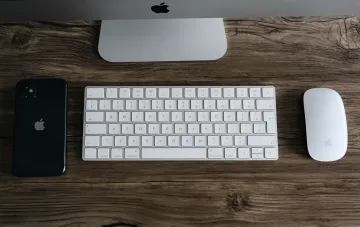 Рабочее место с iPhone, клавиатурой и мышью Apple на деревянном столе — символ программы Trade In с повышенными выплатами до $1300