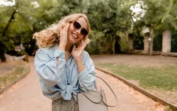 Счастливая женщина в солнцезащитных очках и стильной одежде, символизирующая финансовый успех и уверенность — иллюстрация к финансовому гороскопу на вторую половину 2026 года