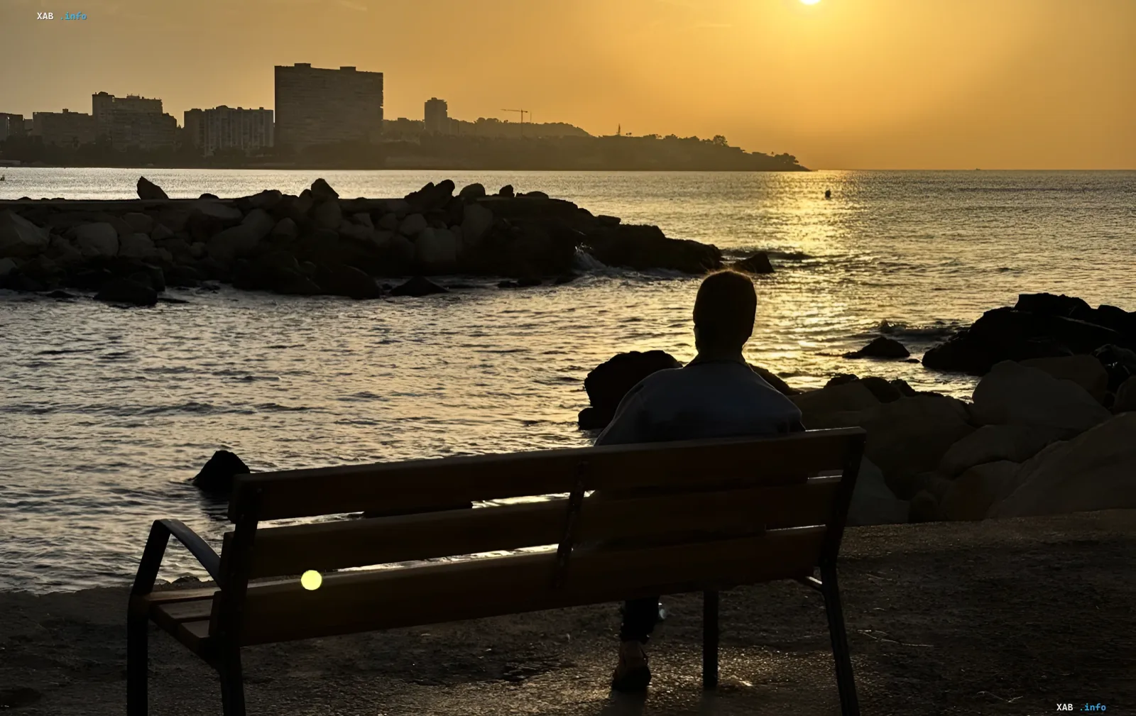 Eine Person sitzt auf einer Bank am Meer bei Sonnenuntergang und genießt die Wärme der Samtsaison 2026