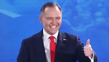 Министр обороны Польши Мариуш Бłaszczak дает знак одобрения на фоне синего экрана