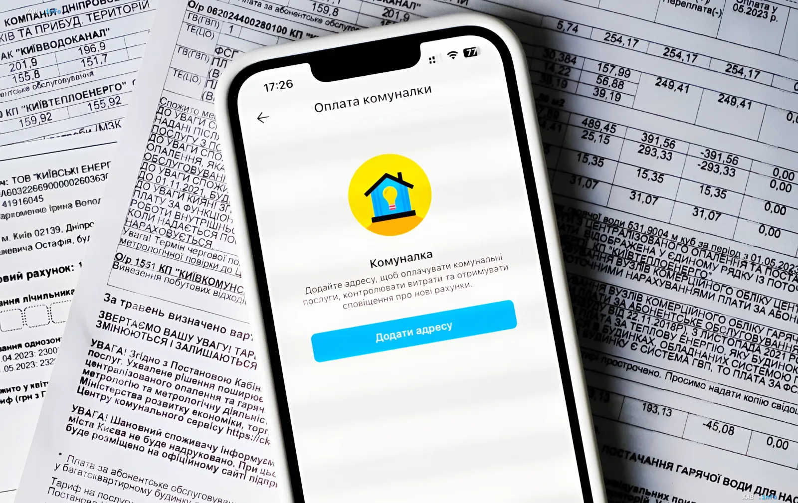 Смартфон с приложением для оплаты коммунальных услуг лежит на фоне счетов за ЖКХ, символизируя проблему долгов за уничтоженное жилье в Украине