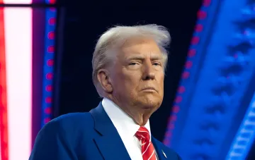 Donald Trump in a blue suit on a debate stage, serious expression — illustrating the news about court halting ballroom construction at the White House