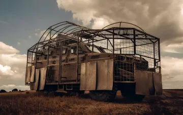 Ukrainisches Militärfahrzeug, geschützt vor FPV-Drohnen mit Metallgitter und Schilden, steht auf einem Feld