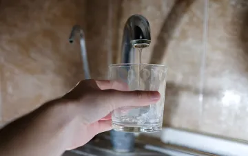 Рука наполняет стакан чистой водой из крана — символ повседневного потребления, которое в Харькове станет дороже в три раза из-за кризиса водоснабжения