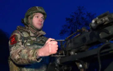 Украинский военнослужащий в камуфляже и шлеме работает с оборудованием ночью, возможно, связанным с ПВО или управлением дронами, в контексте атаки на Киев и Днепр