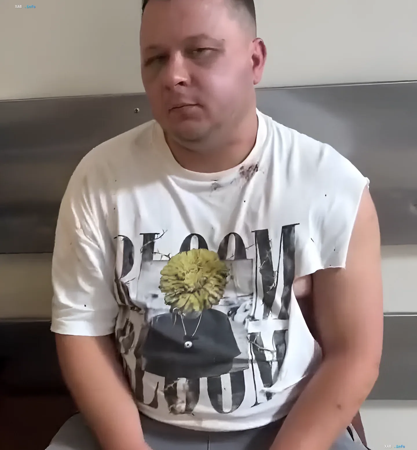 Чоловік у білій футболці з принтом, що сидить у приміщенні, можливо, учасник інциденту з аніматором та військкоматом у Харкові