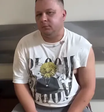 Mann in einem weißen T-Shirt mit Druck, sitzend in einem Raum, möglicherweise beteiligt am Vorfall mit einem Animator und dem Militärregistrierungsamt in Charkiw