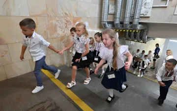 Schoolchildren in uniform descend stairs in the metro, symbolizing the dangerous journey to school in Kyiv due to shelling