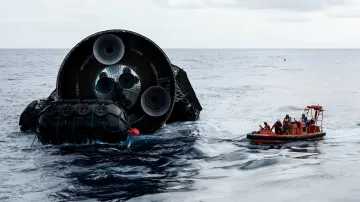Буксировка уцелевшего Starship Ship 40 в Индийском океане: оранжевая спасательная лодка тянет огромный черный корпус ракеты с видимыми двигателями, окруженный волнами и спасательными кругами