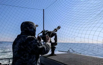 Ukrainian Navy sailor in camouflage operates an anti-aircraft machine gun on a ship deck in the Black Sea — symbol of defense against Russian drones after strike on 'Sivash'